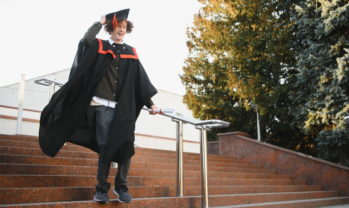 Happy graduation student walking down stairs in cap and gown.