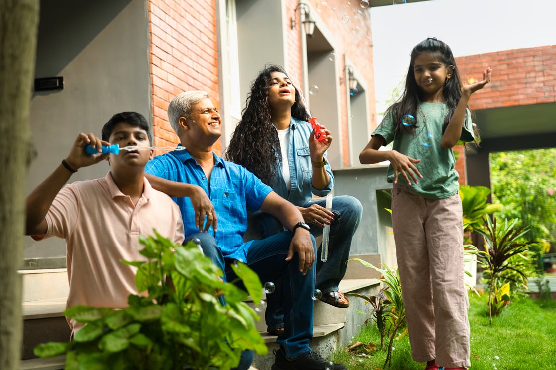 Family sitting on back steps of their home blowing bubble in the summer.