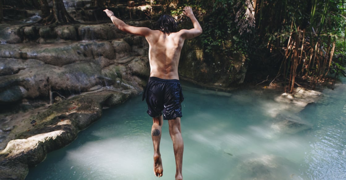 Young man jumping into waterfall lake