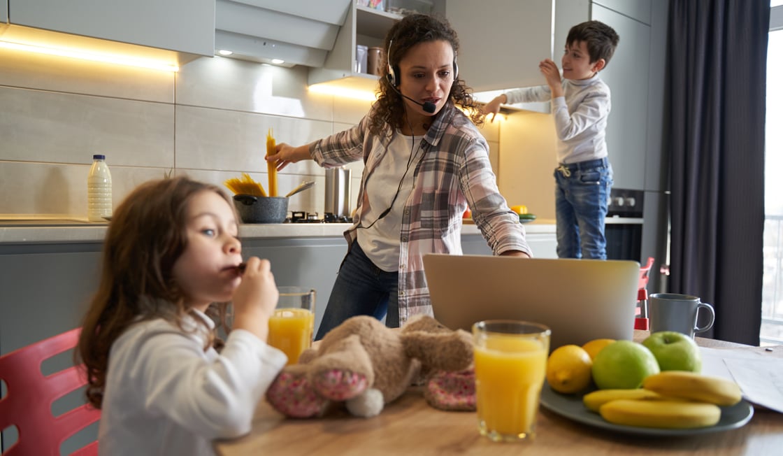 Mother busy in the kitchen trying to work on computer with kids climbing around the kitchen