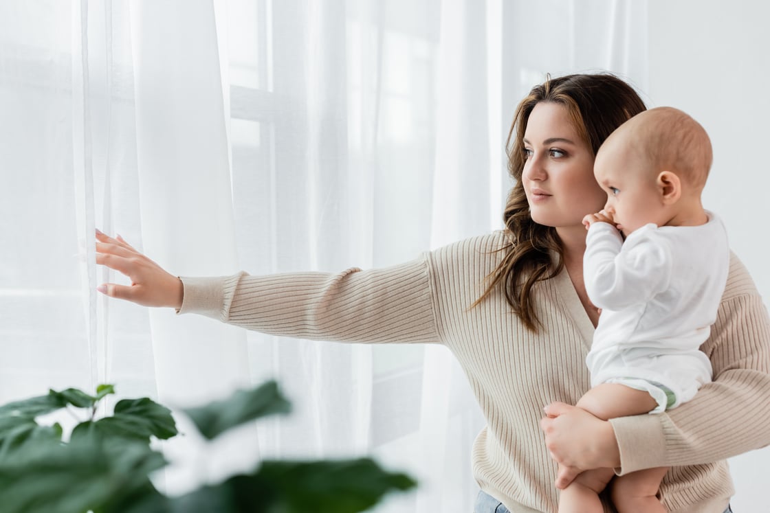 Peaceful young mother holding baby and looking out the window